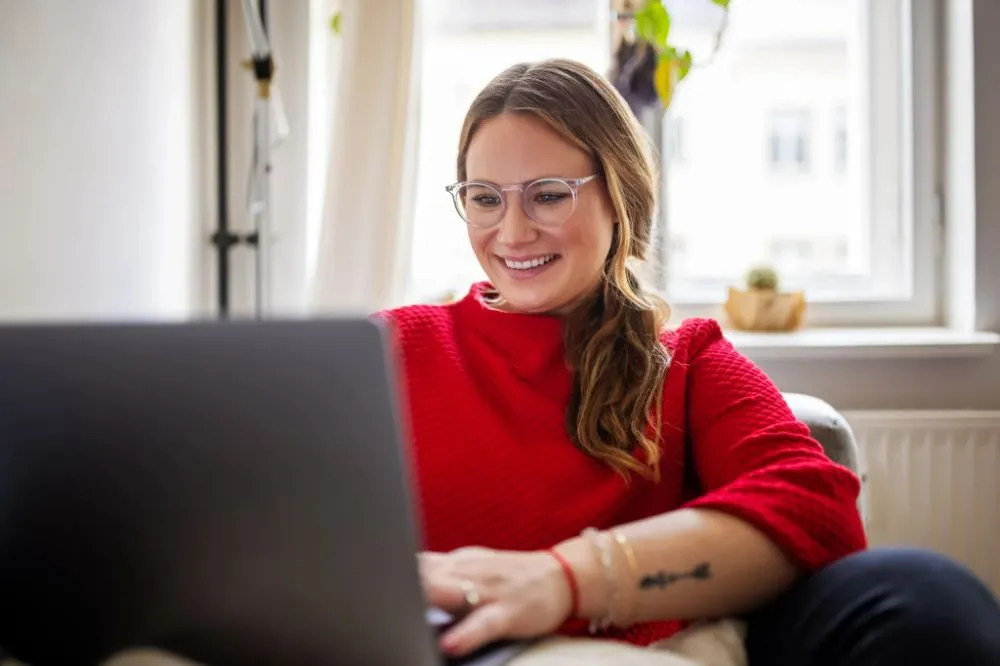 A woman smiling while browsing on her laptop at home.